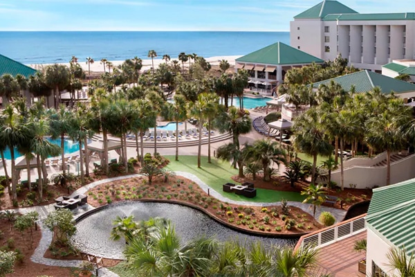 Aerial view of The Westin Hilton Head Island Resort & Spa with a fountain, pool, tall palm trees, and ocean in the background