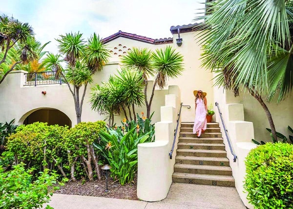 Woman in sundress and beach hat walking down the adobe stairs of the Estancia La Jolla Hotel & Spa